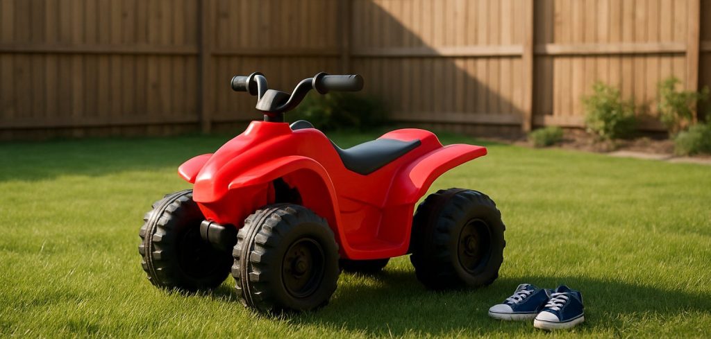 A small red toddler ride-on quad parked on a flat, fenced backyard lawn next to a pair of toddler sneakers